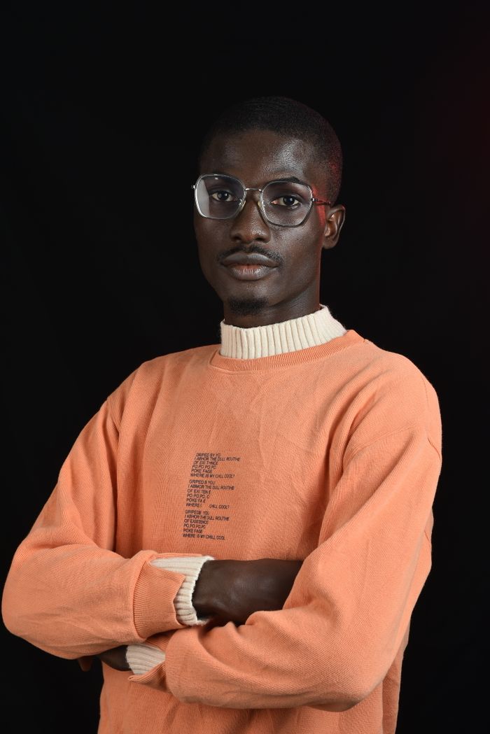 services-03 Confident young man in an orange sweater and glasses posing against a black background.